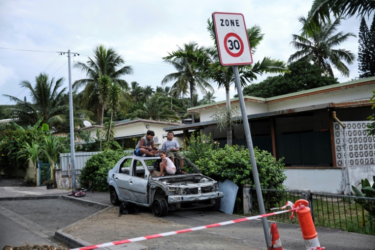 Des enfants sont assis sur la carcasse d'une voiture après la sécurisation du quartier de Logicoop par les forces de l'ordre, le 29 mai 2024 à Nouméa
