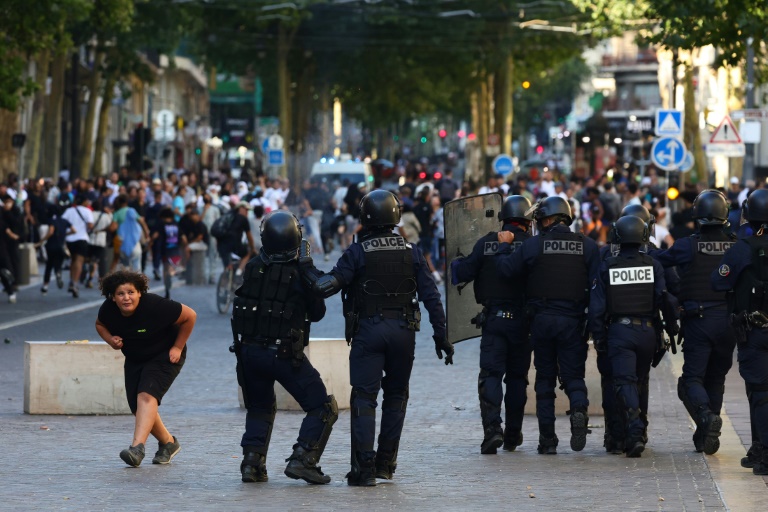 Une jeune fille se baisse en passant devant des policiers qui se préparent à disperser des manifestants avec des gaz lacrymogènes à Marseille le 1er juillet 2023, après une quatrième nuit d'émeutes en France à la suite de la mort de Nahel par un tir policier