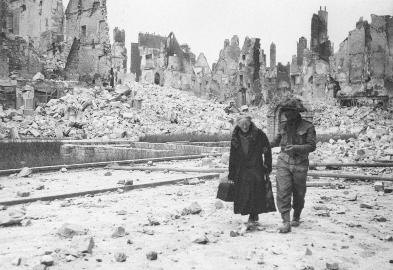 Un soldat américain aide une femme âgée dans la ville de Caen complètement détruite par les bombardements en juin 1944, pendant la Seconde Guerre mondiale