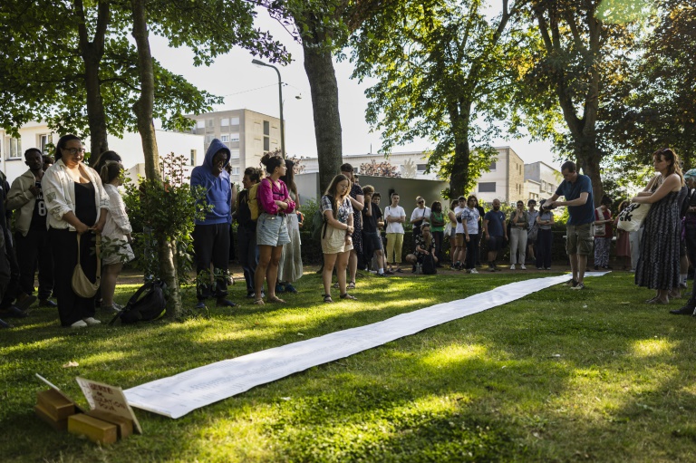 Hommage aux migrants morts lors d'une tentative de traversée de la Manche dont les noms sont inscrits sur un longue feuille de papier, le 19 juillet 2024 à Calais