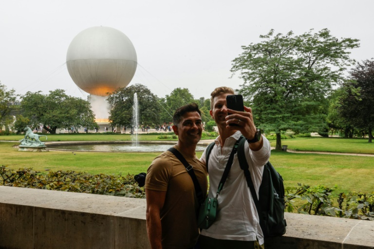 Des visiteurs se prennent en photo devant la vasque olympique aux allures de montgolfière posée dans le jardin des Tuileries, le 27 juillet 2024 à Paris