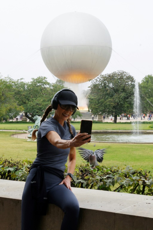 Une femme prend un selfie devant la vasque olympique aux allures de montgolfière posée dans le jardin des Tuileries, le 27 juillet 2024 à Paris