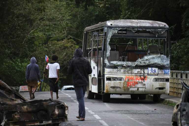 Des manifestants indépendantistes kanaks près d'un bus endommagé et des véhicules calcinés alors qu'ils bloquent le pont menant au village de Houaïlou, sur la côte est de la Nouvelle-Calédonie, le 1er juillet 2024