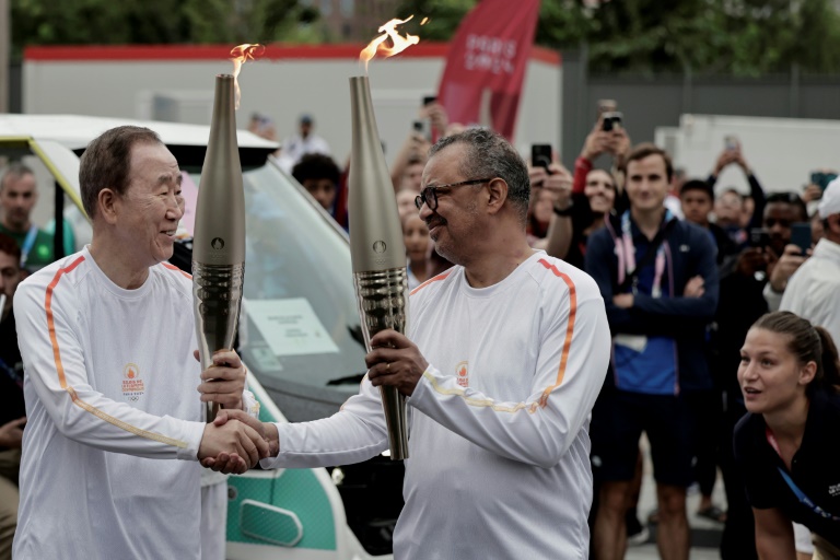 L'ancien secrétaire général des Nations Unies Ban Ki-moon (à gauche) et le directeur général de l'Organisation mondiale de la santé (OMS) Tedros Adhanom Ghebreyesus (à droite) se serrent la main lors du passage de relais de la flamme olympique dans le cadre des JO de Paris, à Saint-Denis (Seine-Saint-Denis), le 26 juillet 2024