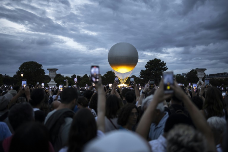 Des visiteurs photographient la vasque des Jeux olympiques et paralympiques de Paris 2024 au coucher du soleil, dans le Jardin des Tuileries, à Paris, le 7 août 2024