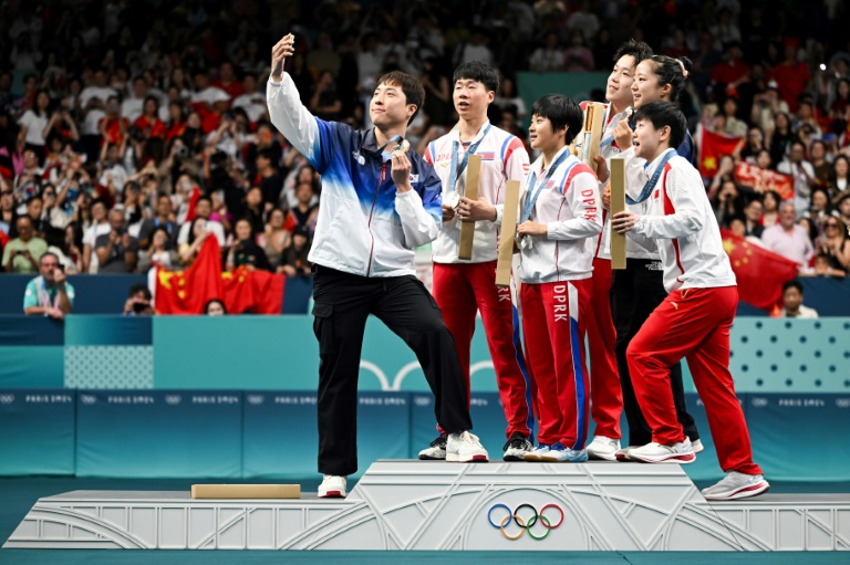 Le Sud-Coréen Lim Jonghoon (g), médaille de bronze, prend un selfie sur le podium avec les Nord-Coréens médaillés d'or Wang Chuqin (derrière, à droite) et Sun Yingsha (devant, à gauche), Ri Jong Sik (2e g) et Kim Kum Yong (c), médaillés d'argent, et sa coéquipière Shin Yubin à l'issue de la compétition de tennis de table mixte en double aux Jeux Olympiques de Paris 2024, le 30 juillet 2024 à l'Arena Paris Sud, à Paris