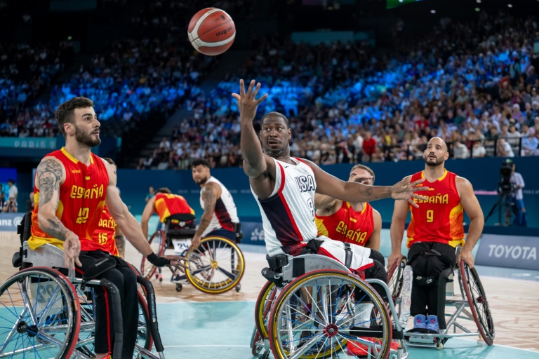 L'Américain Brian Bell (c) passe le ballon sous le regard de L'Espagnol Manuel Lorenzo (g) pendant le tour préliminaire du groupe B du match de basket-ball en fauteuil roulant entre les États-Unis et l'Espagne pendant les Jeux paralympiques de Paris 2024 à Paris, le 29 août 2024