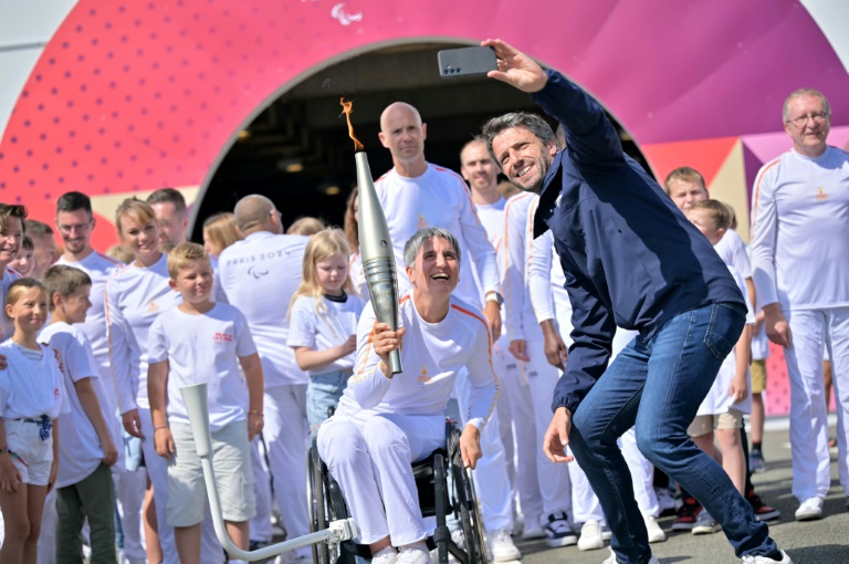 Le président du Comité d'organisation des Jeux (Cojo) Tony Estanguet (D) prend un selfie avec Emmanuelle Assmann porteuse de la flamme paralympique, le 25 août 2024 à Coquelles dans le Pas-de-Calais