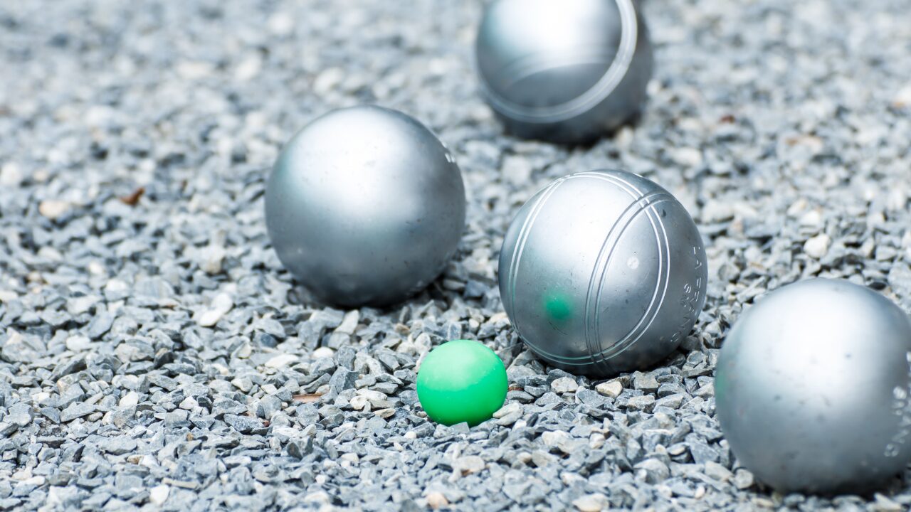 Au sol, 4 boules de pétanque métalliques entourent un cochonnet vert.