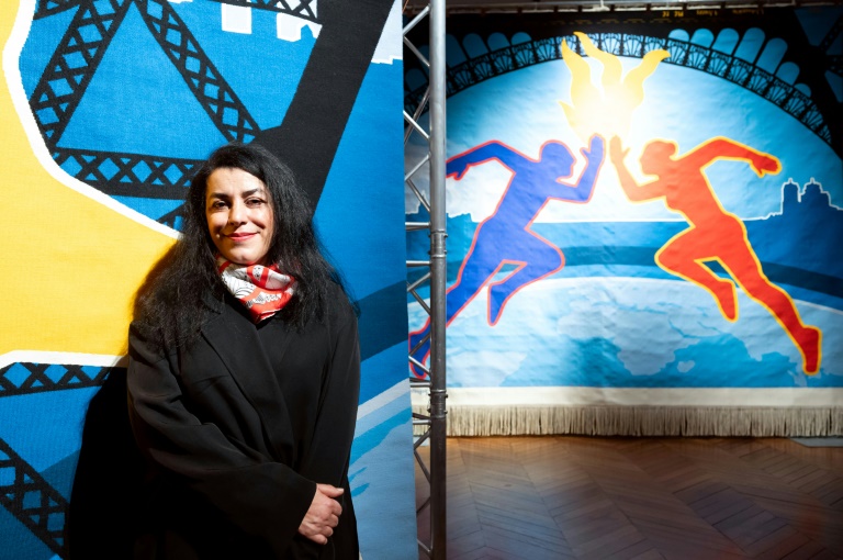 Marjane Satrapi pose le 12 mars 2024 devant l'un des trois éléments de la tapisserie officielle qu'ele a conçue pour les Jeux de Paris-2024. L'autrice de bandes dessinées et réalisatrice franco-iranienne sera au nombre des porteurs de la flamme paralympique le 25 août à Paris