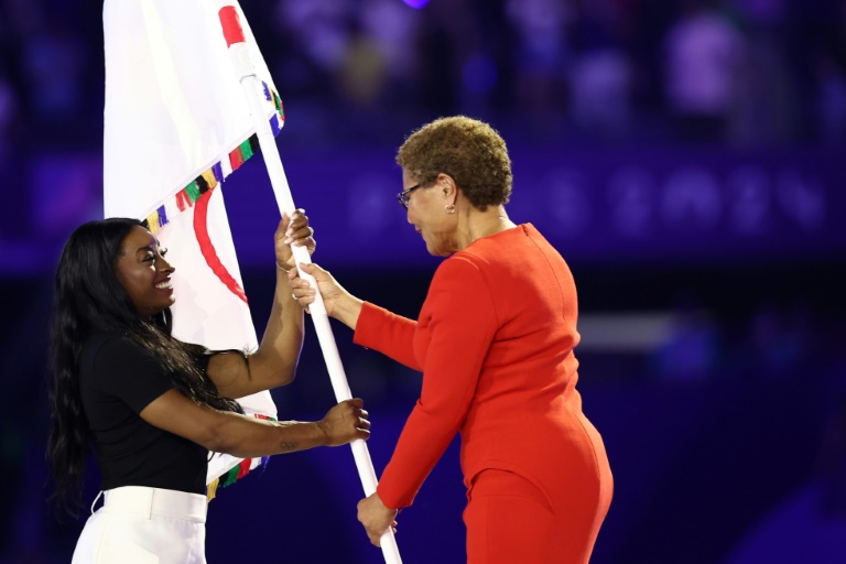 La maire démocrate de Los Angeles, Karen Bass (d) remettant le drapeau olympique à la gymnaste américaine Simone Biles (g) lors de la cérémonie de clôture des Jeux olympiques de Paris 2024 au Stade de France, le 11 août 2024