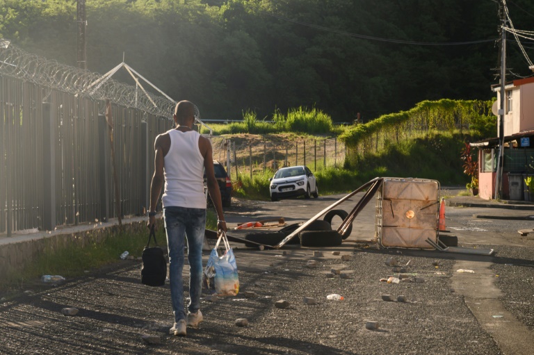 Un habitant chargé de sacs de provisions passe à côté de débris après des violences à Fort-de-France, le 23 septembre 2024 en Martinique