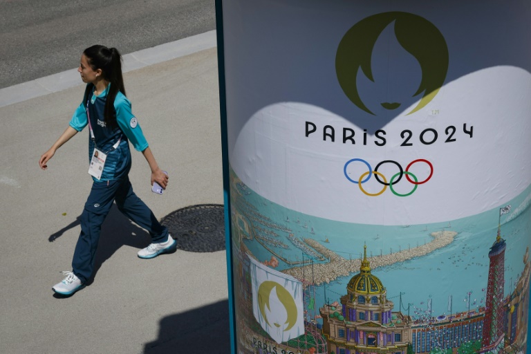 Une volontaire passant à côté d'une affiche des Jeux olympiques 2024 dans le village des athlètes le 18 juillet 2024 à Saint-Denis