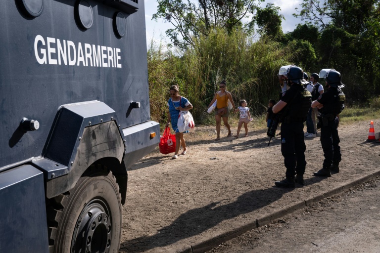 Des habitants chargés de provisions passent à côté de gendarmes stationnés à un barrage routier à Saint-Louis, au sud de Nouméa, le 23 septembre 2024 en Nouvelle-Calédonie