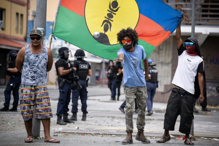 Des habitants indépendantistes jouent à la pétanque, tout en déployant un drapeau du FLNKS, sous le regard des forces de sécurité à Nouméa, dans le quartier de la valllée du Tir, le 24 septembre 2024