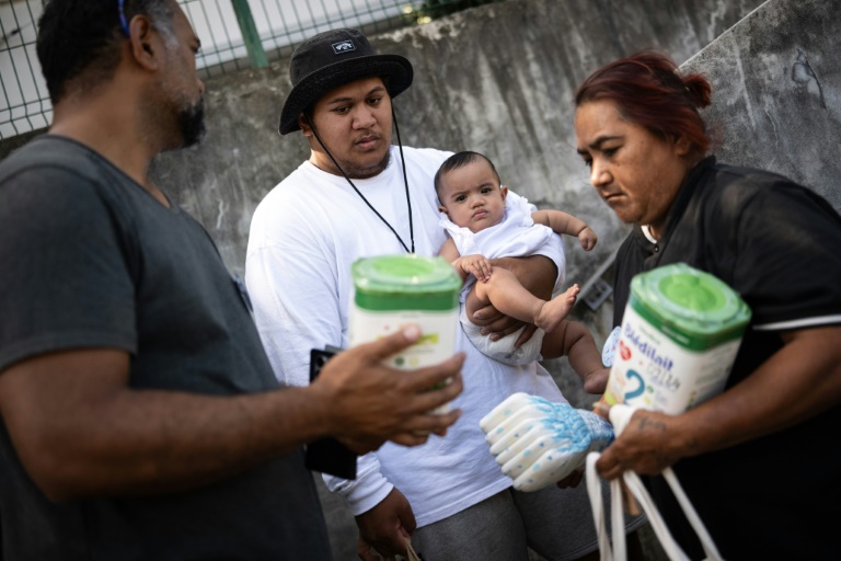 Jean-Baptiste Maukava (c) reçoit de l'aide alimentaire distribuée par Francis Maluia (g), dans le quartier de Rivière Salée à Nouméa, le 26 septembre 2024 en Nouvelle-Calédonie