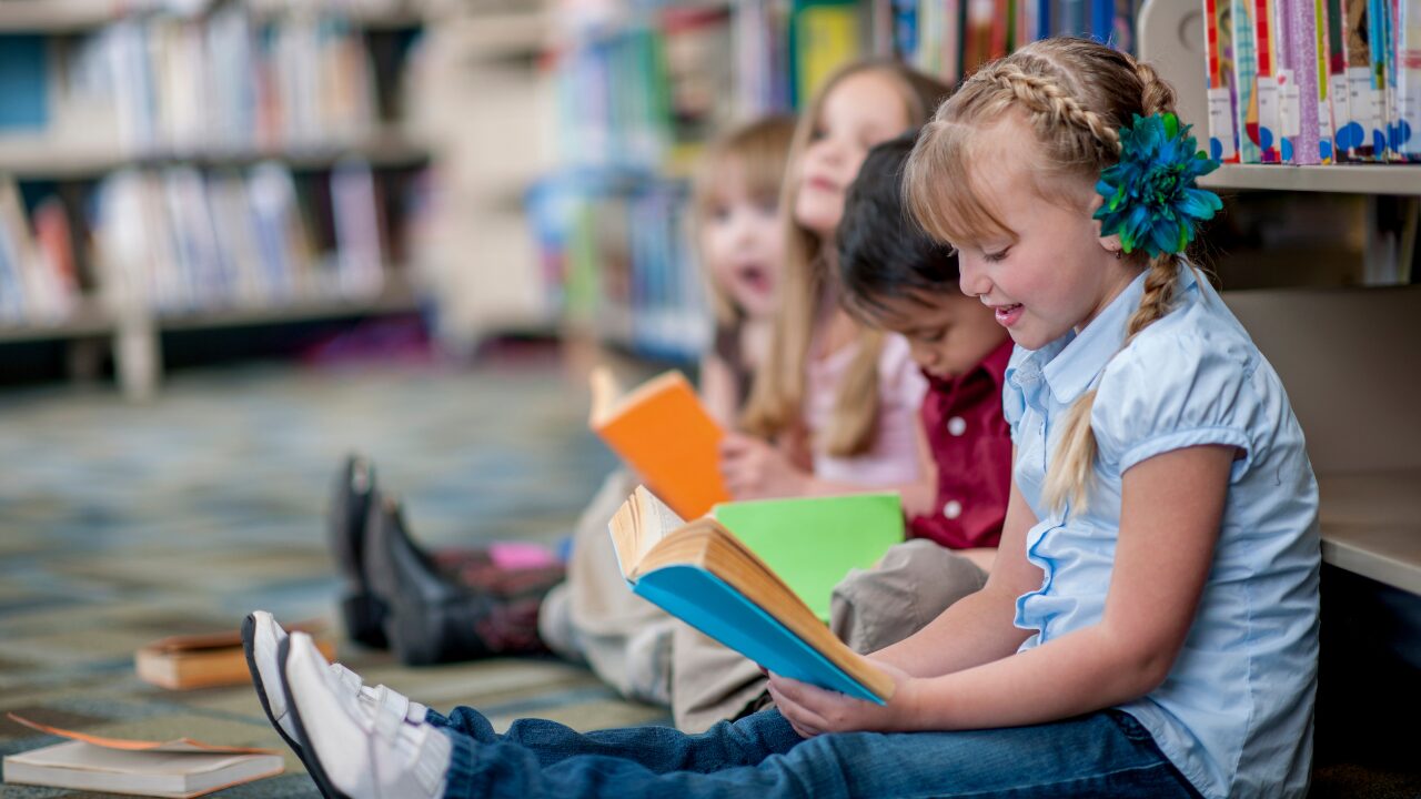 Dans une libraire, des enfants sont assis par terre et lisent chacun un livre.