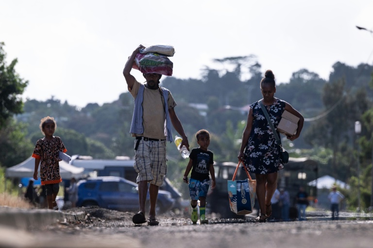 Des habitants chargés de provisions passent près d'un barrage routier de la gendarmerie à Saint-Louis, au sud de Nouméa, le 23 septembre 2024 en Nouvelle-Calédonie