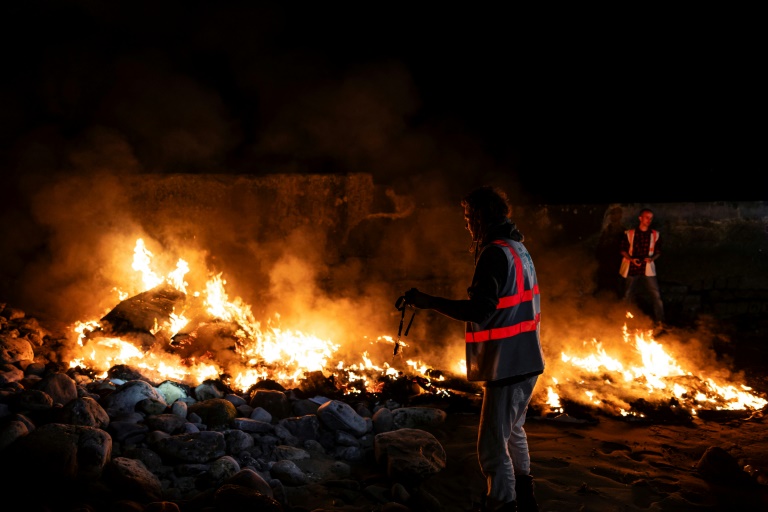 Thomas Chambon (C), coordinateur de l'association Utopia 56, et Nikolaï Posner, un bénévole et ancien salarié d'Utopia 56, près d'un canot en feu sur la plage du Portel (Pas-de-Calais) le 21 septembre 2024