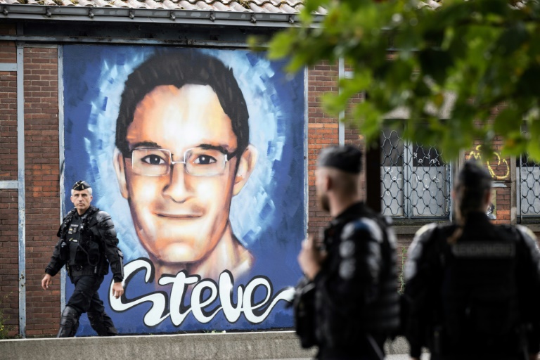 Des policiers anti-émeutes se tiennent, le 21 juin 2022 à Nantes, à côté d'une peinture murale en hommage à Steve Maia Canico, qui s'est noyé après une intervention de la police lors de la Fête de la musique en 2019