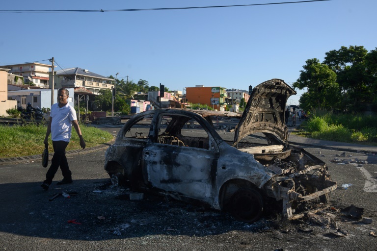 Un habitant passe à côté d'une carcasse de voiture brûlée à Fort-de-France, le 23 septembre 2024 en Martinique