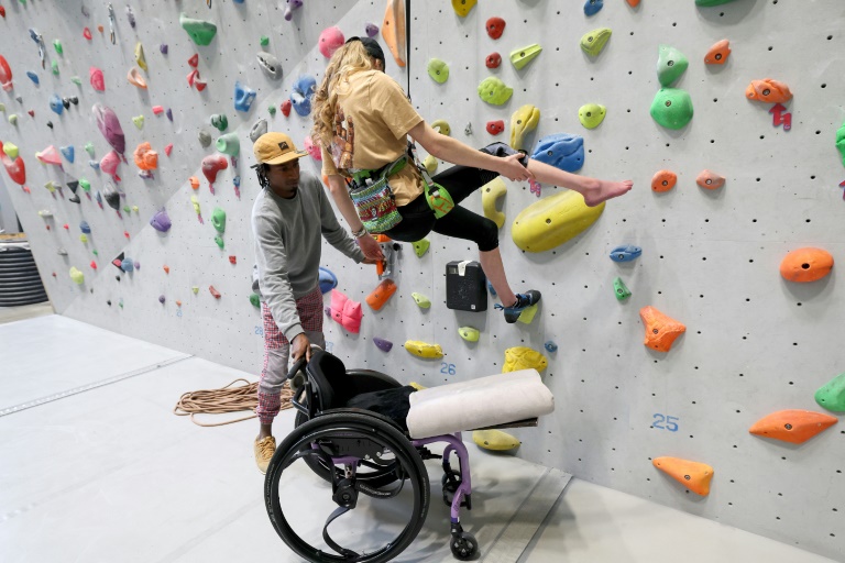 Le champion du monde d'escalade Mickael Mawem (G) aide une personne à utiliser l'assistance électrique lui permettant de grimper, dans une salle de Colmar, le 10 octobre 2024