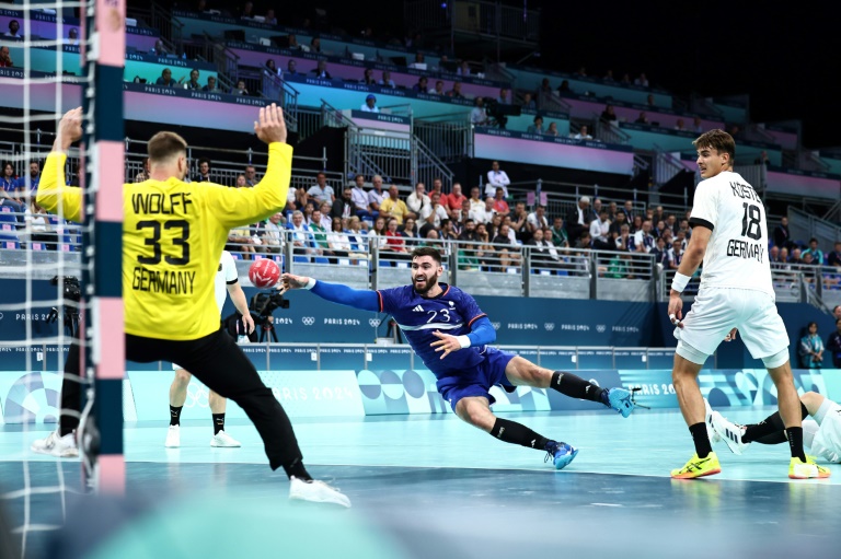 Le pivot français Ludovic Fabregas (c) dépasse l'arrière gauche allemand Julian Koester et tire lors du quart de finale de handball masculin entre l'Allemagne et la France au Jeux olympiques de Paris 2024, au stade Pierre-Mauroy de Villeneuve-d'Ascq, le 7 août 2024 dans le Nord