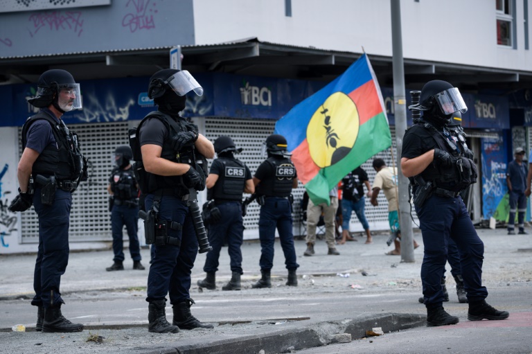 Un drapeau du FLNKS près d'une patrouille des Compagnies républicaines de sécurité (CRS) dans le quartier de La vallée du tir à Nouméa, lors de la fête de la citoyenneté en Nouvelle-Calédonie, le 24 septembre 2024