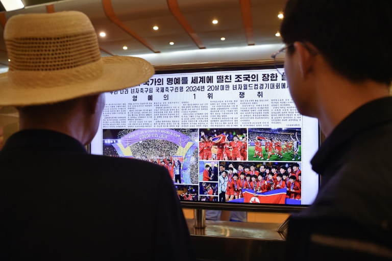 Des passants lisent une édition du quotidien Rodong Sinmun relatant la victoire des Nord-Coréennes lors du Mondial des moins de 20 ans, le 24 septembre 2024 dans le métro de Pyongyang