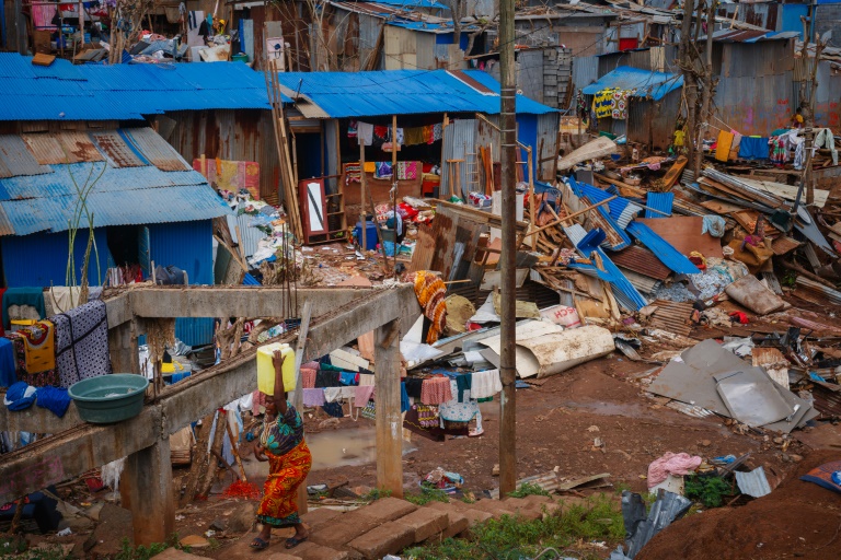 Une habitante du bidonville de Kawéni porte un bidon d'eau au milieu des débris de maisons détruites par le passage du cyclone Chido à Mayotte, le 20 décembre 2024 à Mamoudzou