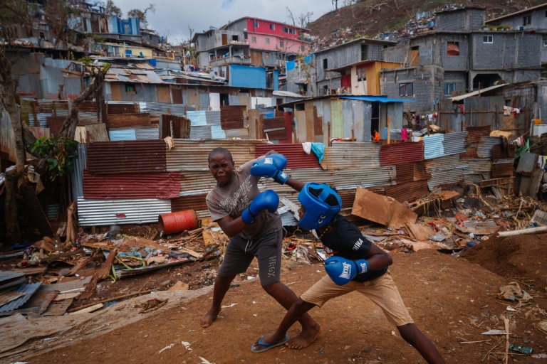 Des jeunes garçons boxent au milieu des débris de maisons détruites par le passage du cyclone Chido à Mayotte, dans le bidonville de Kawéni, le 20 décembre 2024 à Mamoudzou