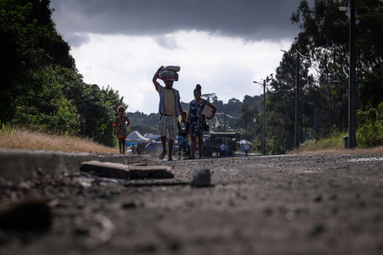 Des piétons passant barrage de gendarmes sur une route en Noucelle-Calédonie aux abords de la ville de Saint-Louis, le 23 septembre 2024