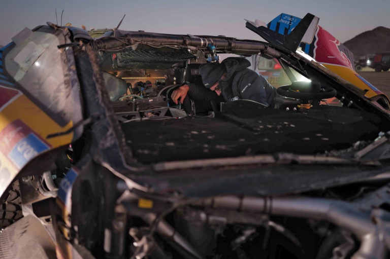 Le tenant du titre en catégorie auto, l'Espagnol Carlos Sainz vérifie l'état de son Ford Raptor très abîmé suite à un accident lors de la premère journée de la 2e étape du Rallye Dakar 2025, en Arabie saoudite, le 5 janvier 2025