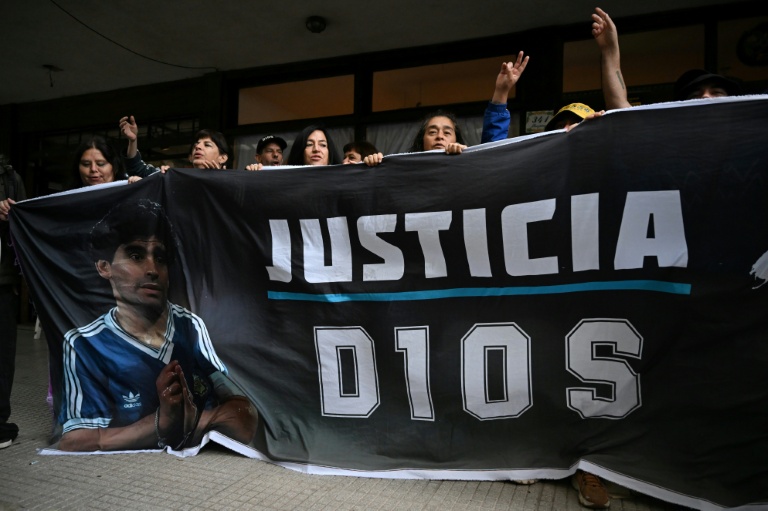 Des fans tiennent un drapeau à l'image du défunt Diego Maradona devant le tribunal de San Isidro, avant le procès concernant la mort de la légende argentine du football à San Isidro, dans la province de Buenos Aires, Argentine, le 11 mars 2025