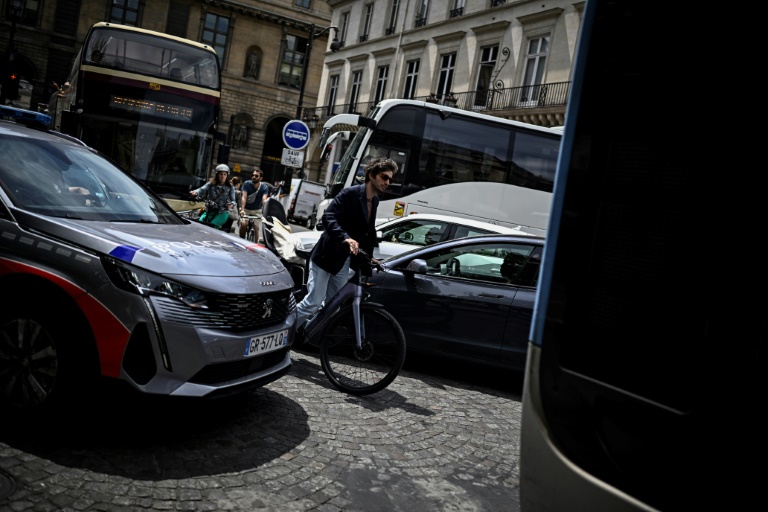 Un homme roule à vélo dans un embouteillage à côté d'une voiture de police dans les rues de Paris, le 28 juin 2024