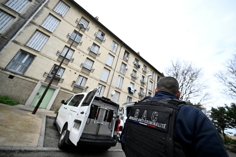 Un policier de la brigade anticriminalité contrôle devant un bâtiment utilisé par des trafiquants présumés dans un quartier d'Avignon, le 13 mars 2025