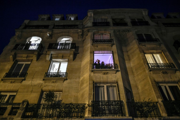 Des personnes se tiennent à leur fenêtre pendant les applaudissements quotidiens de 8 heures en soutien aux soignants, le 27 mars 2020 à Paris, au onzième jour d'un confinement visant à freiner la propagation du Covid-19 en France